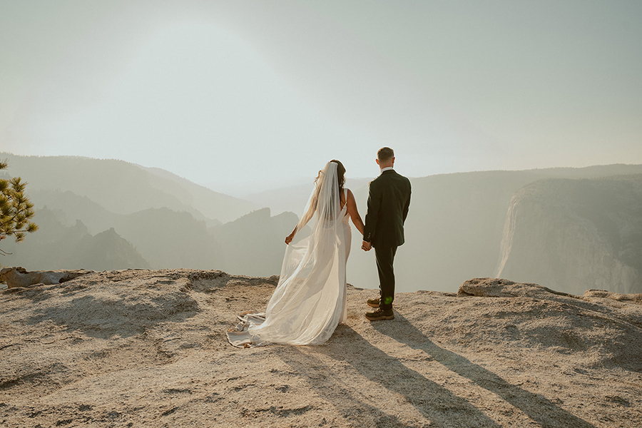 bride and groom standing on a cliff during their yosemite wedding at glacier point